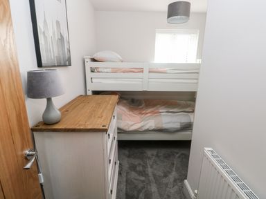 A small bedroom with bunk beds a chest of drawers with a lamp and a window at LunaRoxx 6 Meadow Gardens Kilgetty