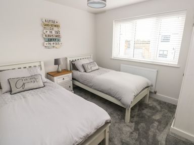 A bedroom with two single beds a nightstand and a window with blinds at LunaRoxx 6 Meadow Gardens Kilgetty