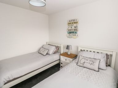 A bedroom with two single beds a nightstand with lamp and wall decor at LunaRoxx 6 Meadow Gardens Kilgetty