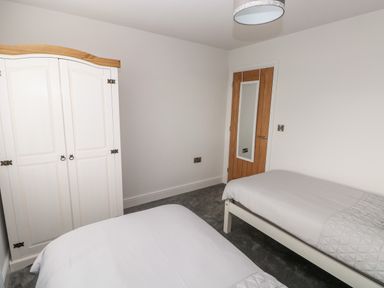 A bedroom with two single beds a white wardrobe a wooden door with a mirror and a ceiling light at LunaRoxx 6 Meadow Gardens Kilgetty