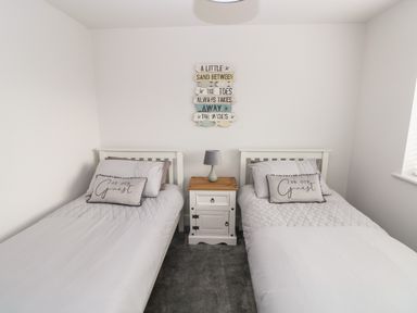 A bedroom with two single beds separated by a nightstand with a lamp and wall decoration at LunaRoxx 6 Meadow Gardens Kilgetty