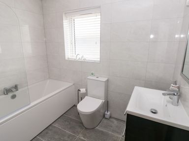 A bathroom with a bathtub toilet and sink under a window at LunaRoxx 6 Meadow Gardens Kilgetty