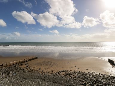 A sandy and rocky beach with wooden groynes under a partly cloudy sky at LunaRoxx 6 Meadow Gardens Kilgetty