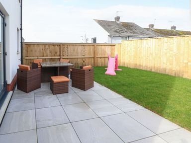 An outdoor patio with a table and chairs next to a grass lawn with a pink slide at LunaRoxx 6 Meadow Gardens Kilgetty