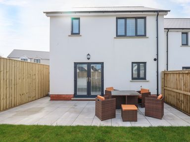 A patio with a table and six chairs outside a two storey house with white walls and black framed windows at LunaRoxx 6 Meadow Gardens Kilgetty
