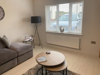 A living room with a gray sofa a black floor lamp two nested round wooden coffee tables and a window showing a parked car at LunaRoxx 6 Meadow Gardens Kilgetty