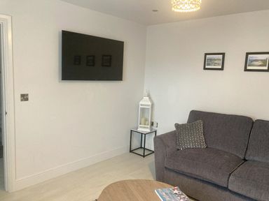 A living room with a mounted TV sofa a side table with candles and two framed pictures on the wall at LunaRoxx 6 Meadow Gardens Kilgetty