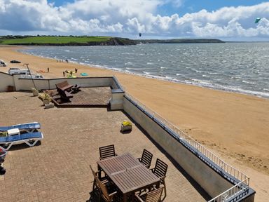 A terrace with a wooden table and chairs and benches overlooking a sandy beach and the sea at High Tide in Duncannon County Wexford
