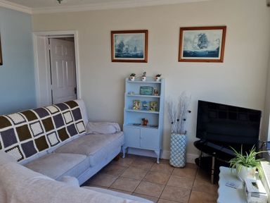 A living room with a sofa a small cabinet with plants framed pictures and a television at High Tide in Duncannon County Wexford