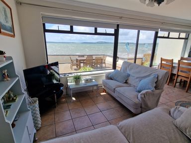 A living room with sofas a television and a dining table overlooking a patio and the sea at High Tide in Duncannon County Wexford