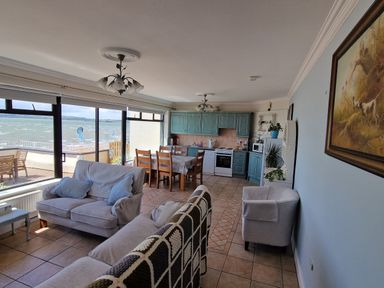 An open living space with sofas a dining table kitchen cabinets and windows overlooking the sea at High Tide in Duncannon County Wexford