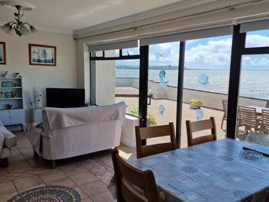 A dining table with chairs and a living room with armchairs and a TV near large windows overlooking a patio and the sea at High Tide in Duncannon County Wexford