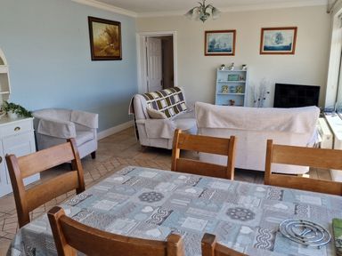 A dining table with wooden chairs in a room with armchairs sofas a television and paintings on the wall at High Tide in Duncannon County Wexford
