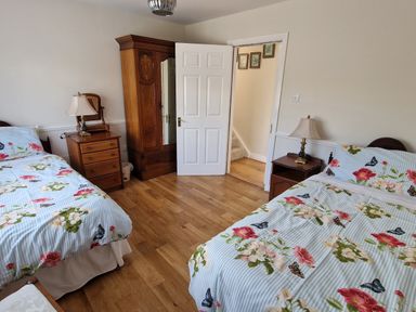 A bedroom with two beds with floral bedding wooden floor wooden wardrobe and two lamps at High Tide in Duncannon County Wexford