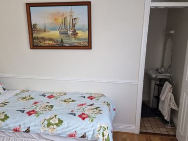 A bedroom with a bed covered in floral bedding and a painting of sailboats on the wall with an open door leading to a small bathroom with a sink and towels at High Tide in Duncannon County Wexford