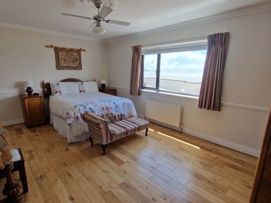 A bedroom with a bed and two bedside tables next to a large window with curtains at High Tide in Duncannon County Wexford