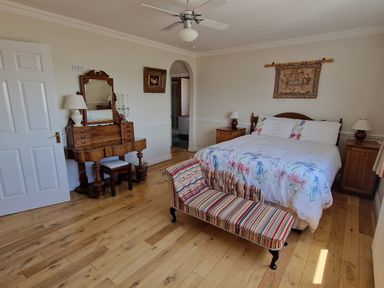 A bedroom with a bed a striped bench a wooden dresser with a mirror and two bedside tables at High Tide in Duncannon County Wexford