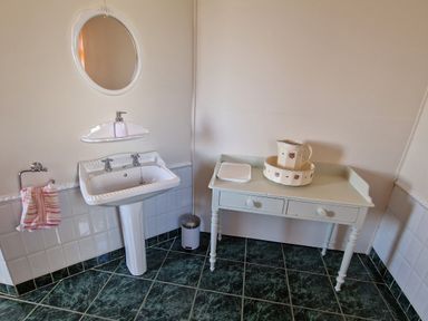 A bathroom with a white pedestal sink a round mirror above and a table with a pitcher and basin at High Tide in Duncannon County Wexford