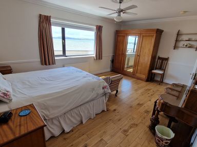 A bedroom with a bed a wooden wardrobe a chair and a window facing water at High Tide in Duncannon County Wexford