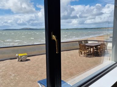 A patio with a wooden table and chairs and a small plant pot overlooking the sea at High Tide in Duncannon County Wexford