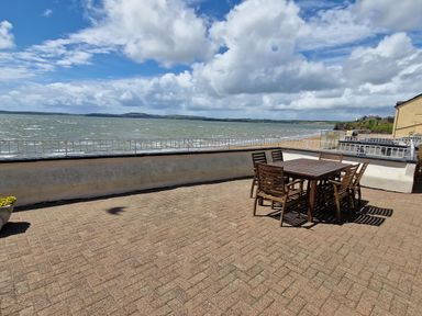 A patio with a wooden table and chairs overlooking a beach and sea at High Tide in Duncannon County Wexford