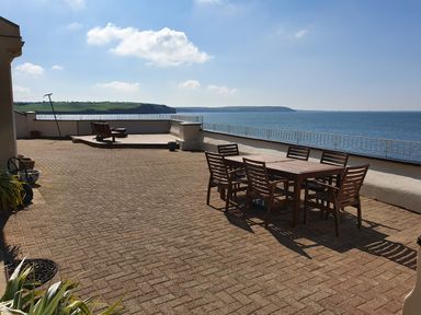 An outdoor patio with a wooden dining table and chairs and lounge chairs overlooking the sea at High Tide in Duncannon County Wexford