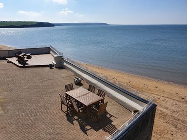 A patio with wooden table and chairs near a beach and ocean at High Tide in Duncannon County Wexford