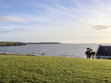 A grassy field overlooking the sea with a house and trees on the right at Beach House in Duncannon County Wexford