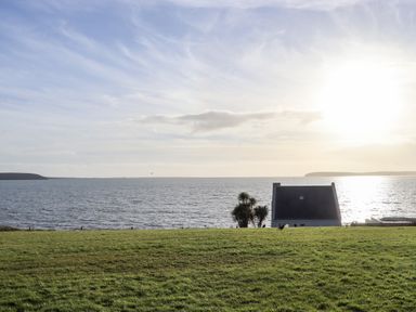 A grassy field overlooking the sea with a white house and trees near the shore at Beach House in Duncannon County Wexford