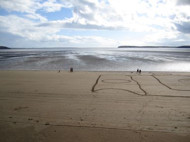 A beach with tide out and people walking near large square and circle patterns drawn in the sand at Beach House in Duncannon County Wexford