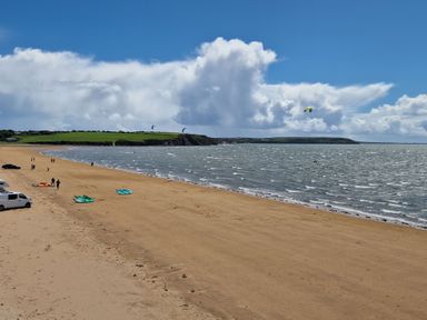 A sandy beach with people and kite surfers on the water and shore at Beach House in Duncannon County Wexford
