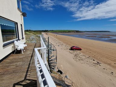 A balcony with two chairs overlooking a sandy beach with a red car and a spiral staircase at Beach House in Duncannon County Wexford