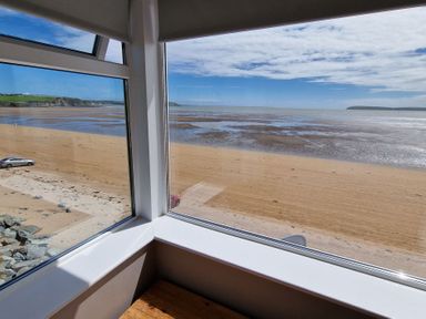 View of a sandy beach and sea from inside a room through corner windows at Beach House in Duncannon County Wexford