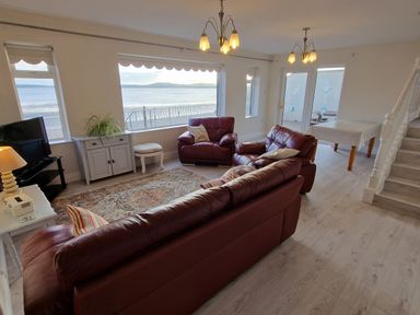 A living room with leather sofas a rug a dining table and large windows overlooking the sea at Beach House in Duncannon County Wexford
