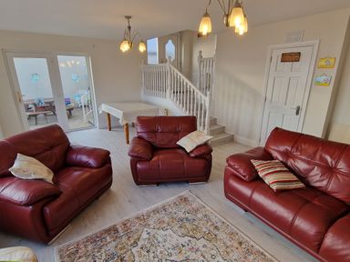 A living room with three red leather sofas a patterned rug a table with a cloth and stairs at Beach House in Duncannon County Wexford