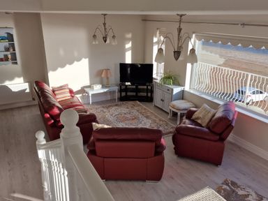 A living room with red leather sofas a television and a large window overlooking the beach at Beach House in Duncannon County Wexford