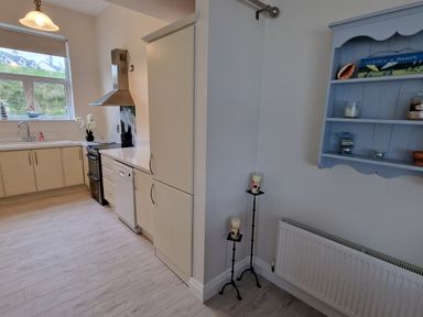 A kitchen with white cabinets dishwasher stove and hood a blue wall shelf and two candle holders at Beach House in Duncannon County Wexford