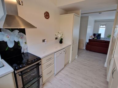 A kitchen with stove dishwasher and cabinets leading to a living room with sofa and TV at Beach House in Duncannon County Wexford