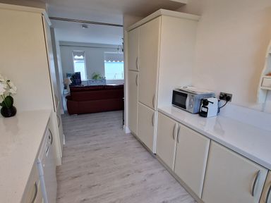 A kitchen with white cabinets a microwave and a coffee machine overlooking a living room with a red sofa and windows at Beach House in Duncannon County Wexford