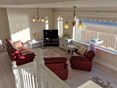 A living room with red leather sofas a television a white cabinet and a large window overlooking the street at Beach House in Duncannon County Wexford
