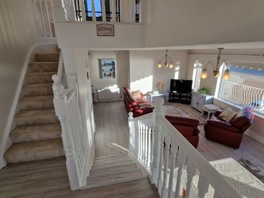 An interior stairway leading down to a living room with red sofas a television and large window at Beach House in Duncannon County Wexford