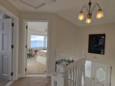 A hallway with a staircase railing and chandelier leading to a bedroom with a large window showing a sea view at Beach House in Duncannon County Wexford