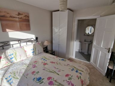 A bedroom with a bed with floral bedding a bedside lamp a white wardrobe and an open door leading to a bathroom at Beach House in Duncannon County Wexford