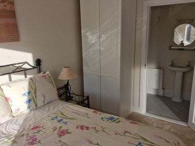 A bedroom with a floral bedspread a bedside table with a lamp a white wardrobe and an adjoining bathroom at Beach House in Duncannon County Wexford