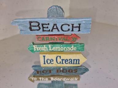 A wooden signpost with arrows labeled Beach Carnival Fresh Lemonade Ice Cream Hot Dogs and To the Boardwalk Beach House Duncannon County Wexford