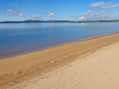 A sandy beach with tire tracks along a calm sea and hills in the distance at Beach House in Duncannon County Wexford