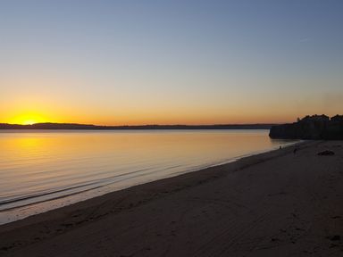 A beach at sunset with calm water and a few people near buildings on a cliff at Beach House in Duncannon County Wexford
