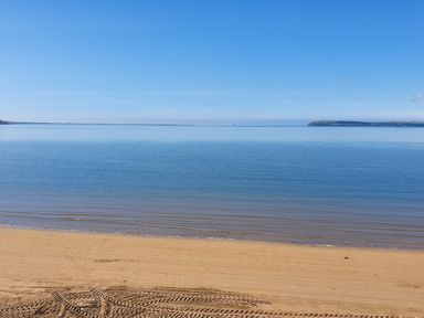 A sandy beach with tire tracks leading to a calm blue sea under a clear blue sky at Beach House in Duncannon County Wexford
