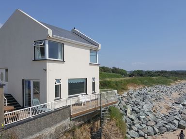 A white two-story house with a balcony overlooking rocky shore and sandy beach at Beach House in Duncannon County Wexford