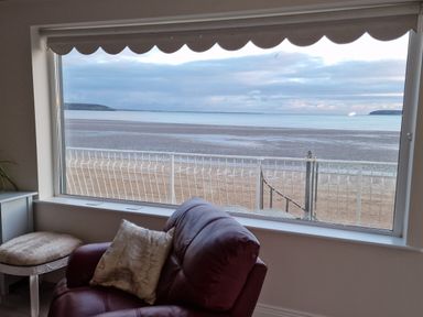 A room with a leather chair a cushion and a small bench facing a large window overlooking a beach and ocean at Beach House in Duncannon County Wexford